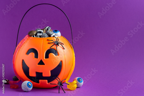 Jack-o-lantern bag full of liquorice candy on purple background with copy space,  horizontal