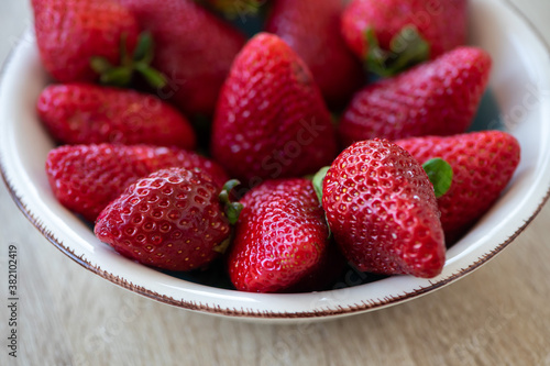 Close-up on a bowl with strawberries on a wooden table.