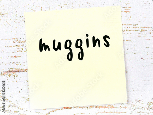 Yellow sticky note on wooden wall with handwritten word muggins photo
