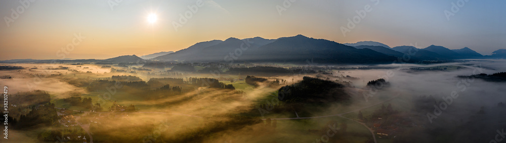 Aerial Panorama view of autumn sunset in mountains with fog and cloud valley landscape. Sun, Haze. Blomberg, Isartal, Bavaria. Dusk