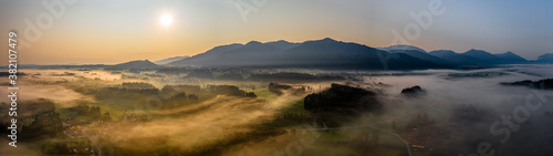 Aerial Panorama view of autumn sunset in mountains with fog and cloud valley landscape. Sun, Haze. Blomberg, Isartal, Bavaria. Dusk