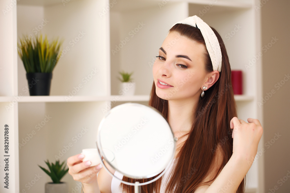 Attractive young woman in bathroom after shower is standing in front of mirror with face cream. Women care. Attractive young woman in bathroom after shower is standing in front of mirror with face cream. Women care.
