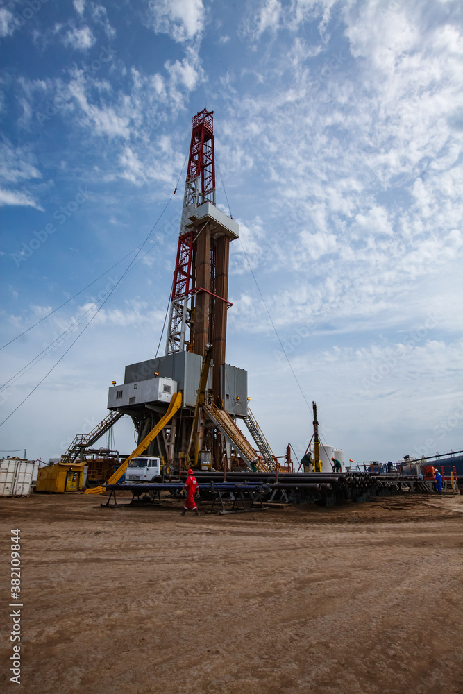 Oil drilling rig and oil worker in red work wear and helmet. Zhaikmunai oil deposit. Uralsk region, Kazakhstan. Oil drilling rig and oil worker in red work wear and helmet. Zhaikmunai oil deposit. Uralsk region, Kazakhstan.