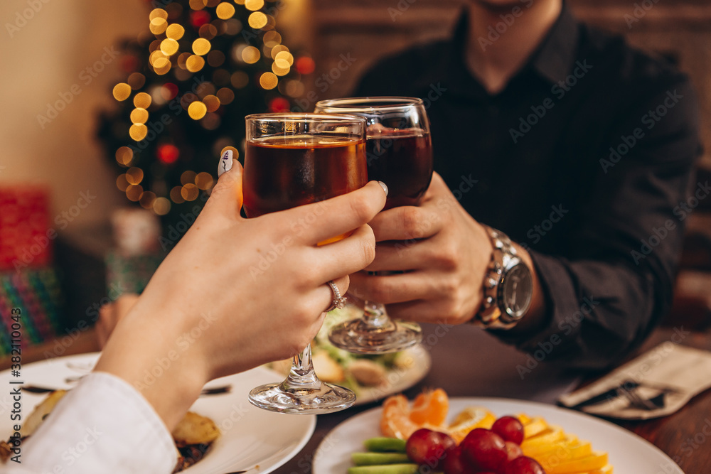 hands with glasses clinking against the background of Christmas tree lights and bonfires from a home fireplace over a table with delicious dishes hands with glasses clinking against the background of Christmas tree lights and bonfires from a home fireplace over a table with delicious dishes