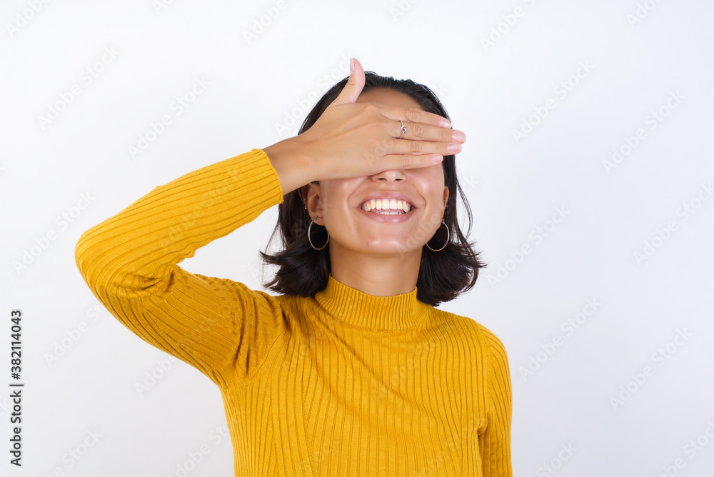 Young hispanic girl with short hair wearing casual yellow sweater isolated over white background smiling and laughing with hand on face covering eyes for surprise. Blind concept. Young hispanic girl with short hair wearing casual yellow sweater isolated over white background smiling and laughing with hand on face covering eyes for surprise. Blind concept.