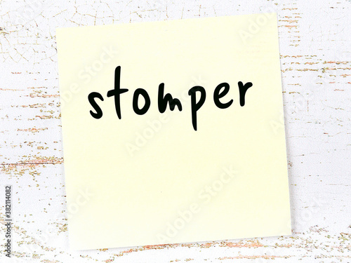 Yellow sticky note on wooden wall with handwritten word stomper photo