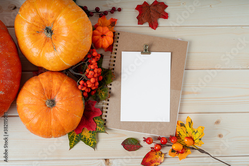 Orange pumpkins, maple leaf, berries and mock up paper blank on wooden background. Hello Fall greeting card, autumn time concept. Flat lay. Copy space.