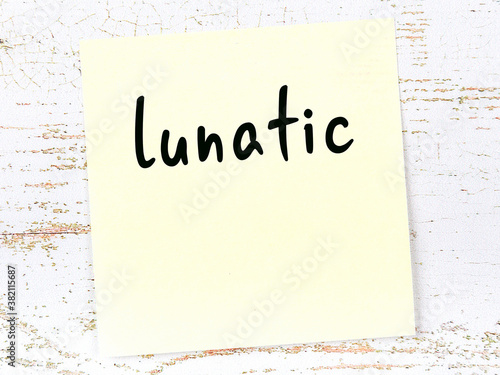 Yellow sticky note on wooden wall with handwritten word lunatic