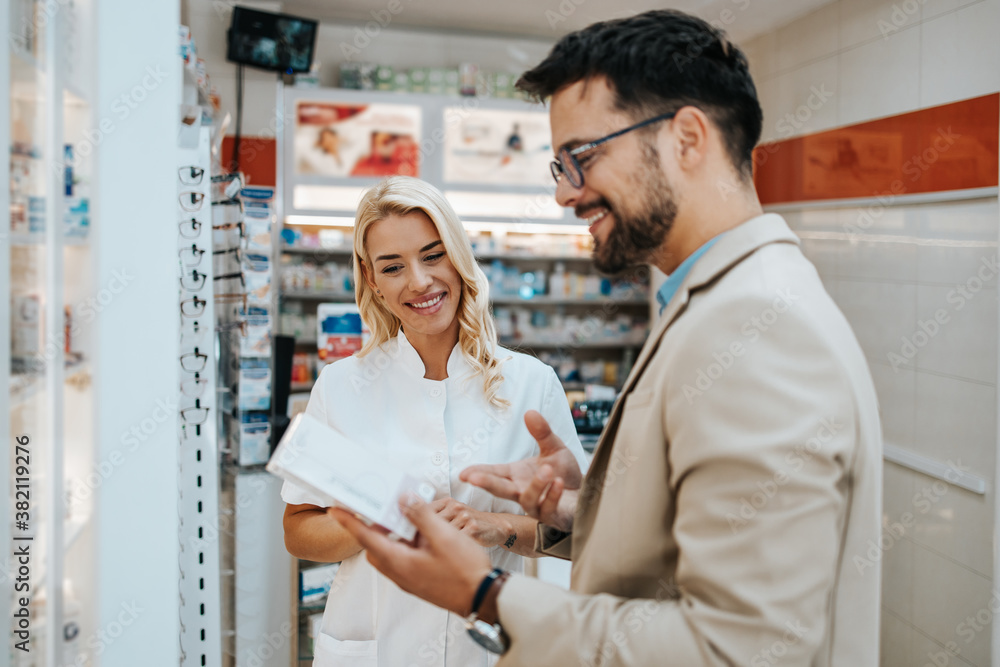 Young business man choosing and buying drugs in a drugstore while talking with attractive female pharmacist. She helping him with expert advices. Young business man choosing and buying drugs in a drugstore while talking with attractive female pharmacist. She helping him with expert advices.