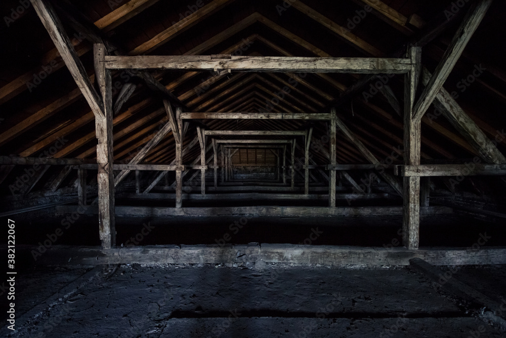 Picture of an old dark and abandoned attic of a residential building with a focus on the decaying framework made of crumbling wooden beams and plywood