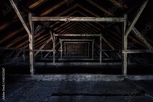Picture of an old dark and abandoned attic of a residential building with a focus on the decaying framework made of crumbling wooden beams and plywood