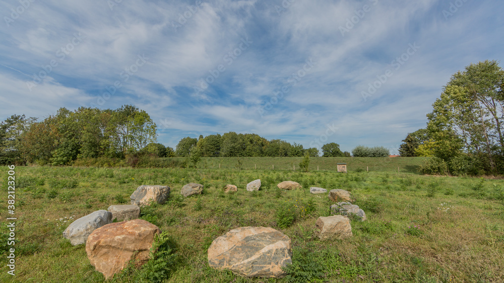 Large stones form a circle between the Dutch countryside with lush trees in the background, sunny spring day at the Itteren recreational pond in South-Limburg in the Netherlands