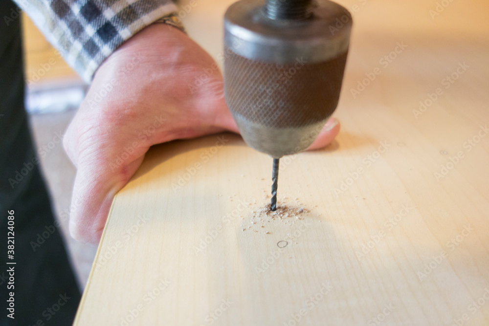 man drilling a hole in wood with an old manual drill