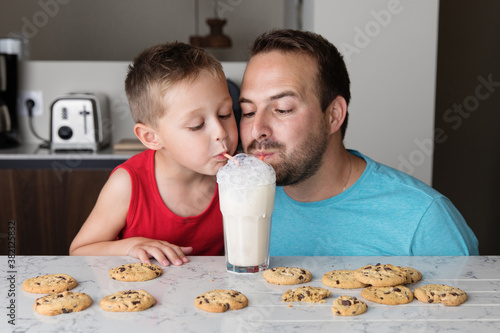 Father and son blowing bubbles in a glass of milk with two straws