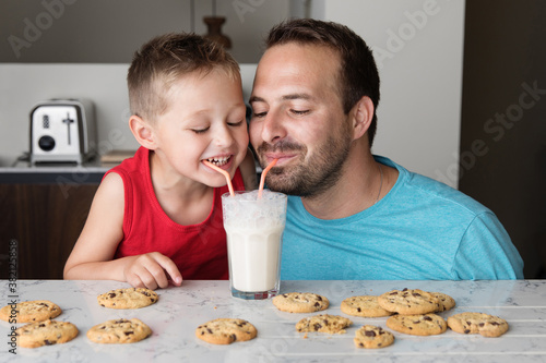 Happy father and son sharing a glass of milk with two straws