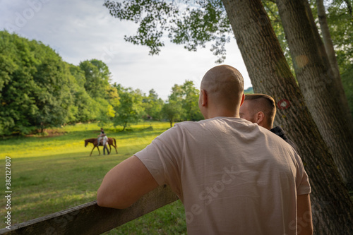 Two muscular guys talking and watching a horse ride