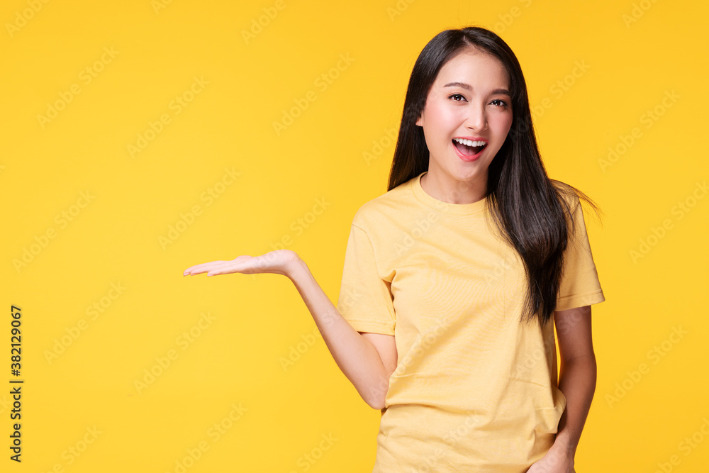 Cheerful young woman holding her hand with product or empty copy space while standing over isolated on yellow background Cheerful young woman holding her hand with product or empty copy space while standing over isolated on yellow background