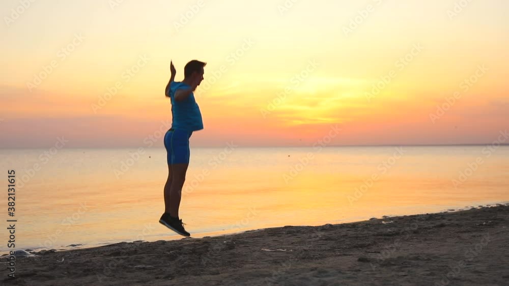 Silhouette young man doing burpees exercise at the sunset sea beach in slowmotion Silhouette young man doing burpees exercise at the sunset sea beach in slowmotion