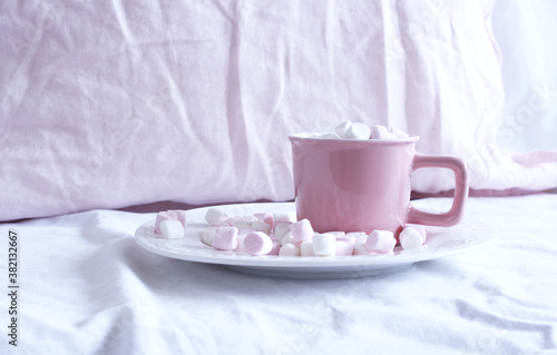 Hot cocoa with marshmallow in a pink ceramic mug on a bed. The concept of holidays and New Year. pink linen background. Flat lay, top view.