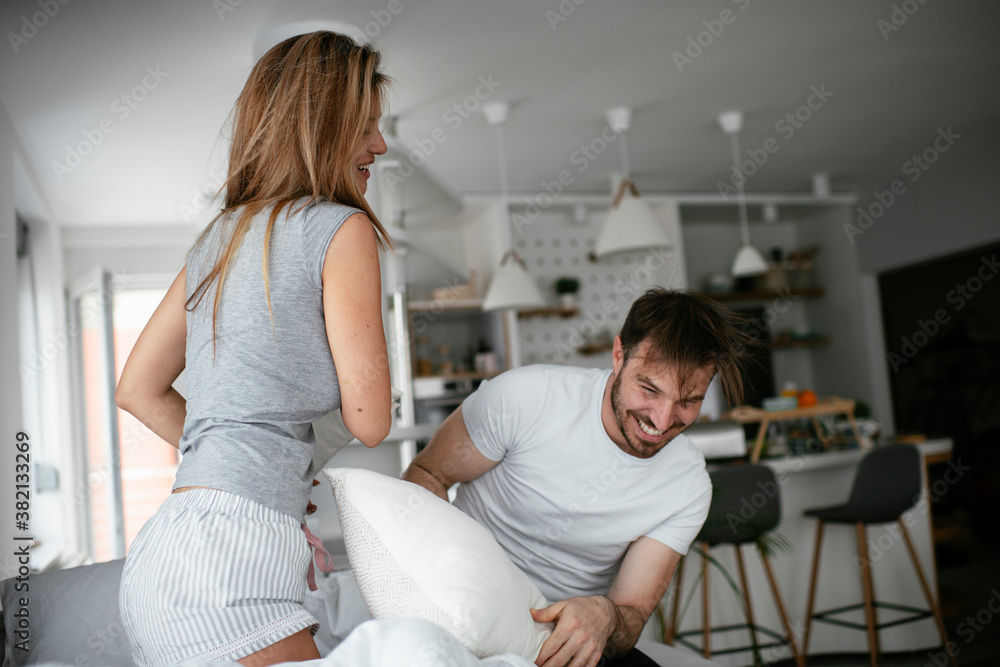 Boyfriend and girlfriend fighting pillows on the bed. Happy couple having fun at home