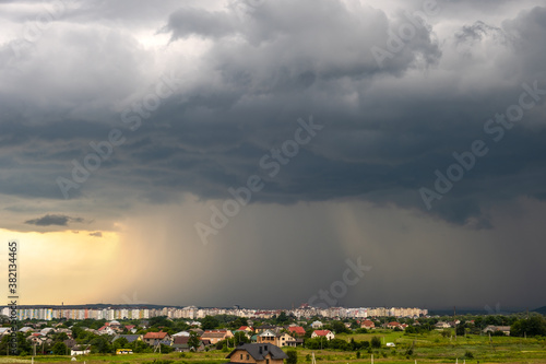 Quadro em tela Moody landscape with dark stormy clouds with falling heavy downpour shower rain over distant town buildings in summer