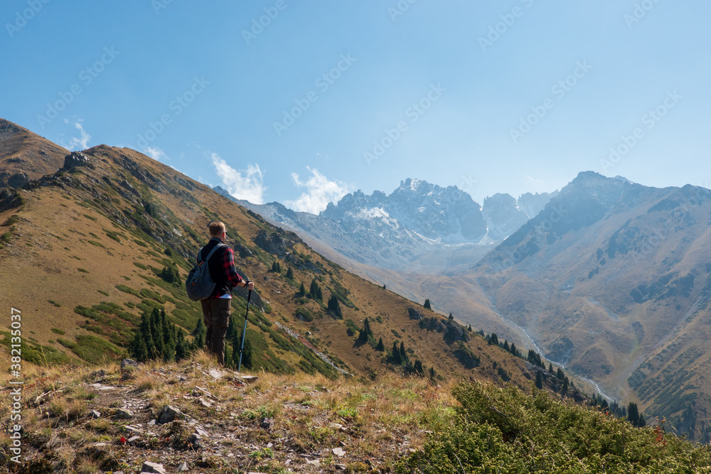 A man with trekking poles and a backpack on the edge of a mountain looking out
