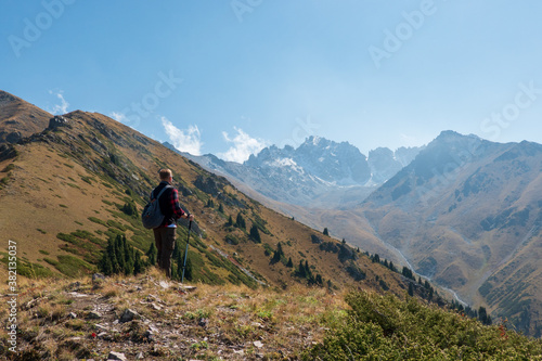 A man with trekking poles and a backpack on the edge of a mountain looking out