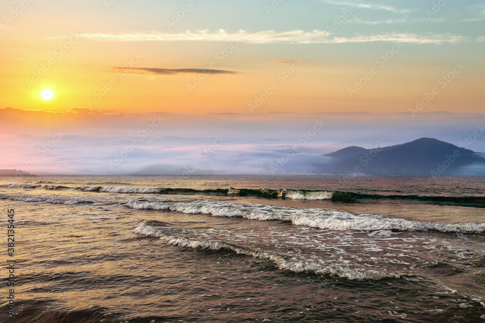 Fototapeta premium Beautiful sunrise in mountains with white fog below and crashing waves of lake water.