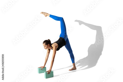 Twin. Beautiful young female athlete stretching, training on white studio background, portrait with shadows. Sportive fit model in motion and action. Flexibility, healthy lifestyle, style concept.