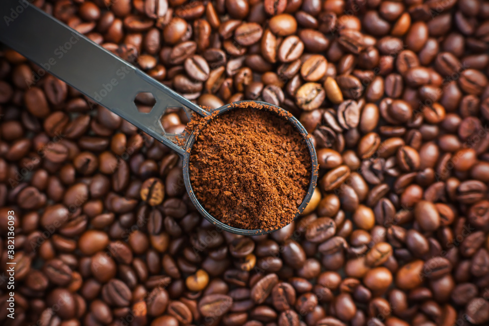 Fototapeta premium On the fragrant coffee beans is a black long measuring spoon, which is filled with ground coffee made from these beans. The view from the top.