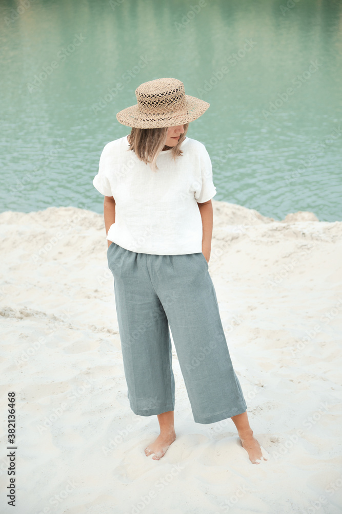 Stylish girl in linen clothes and straw hat. Relaxing in beach, simple slow life style
