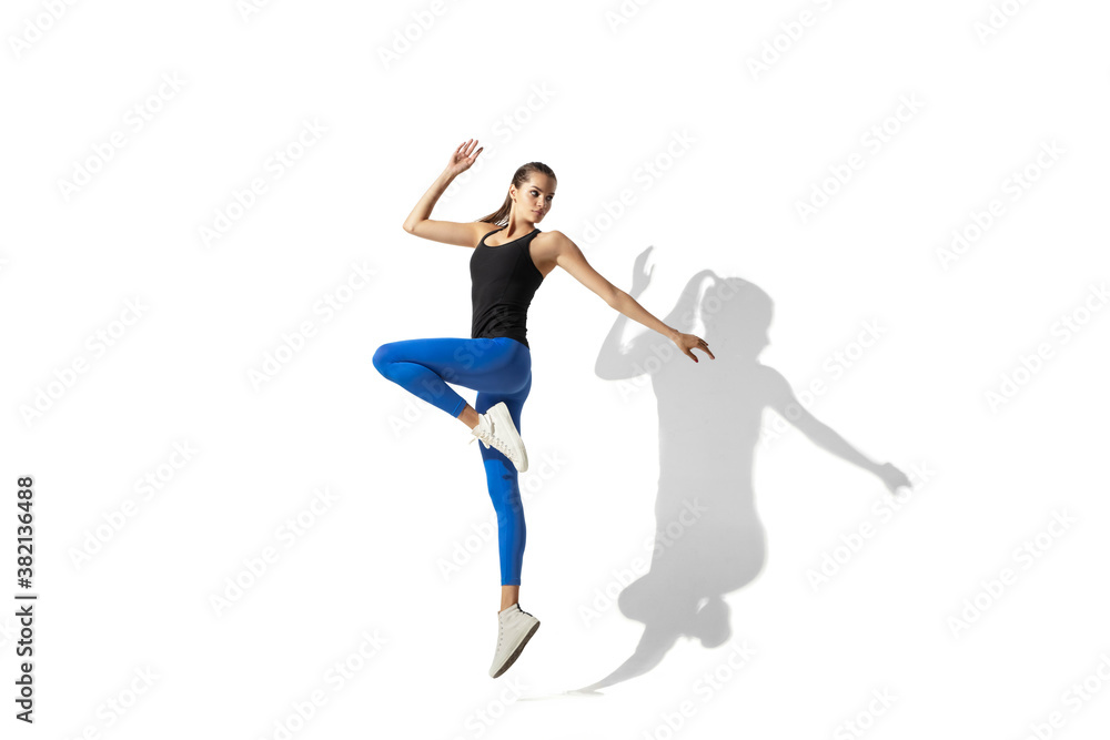 High jump. Beautiful young female athlete stretching, training on white studio background, portrait with shadows. Sportive fit model in motion and action. Flexibility, healthy lifestyle, style concept