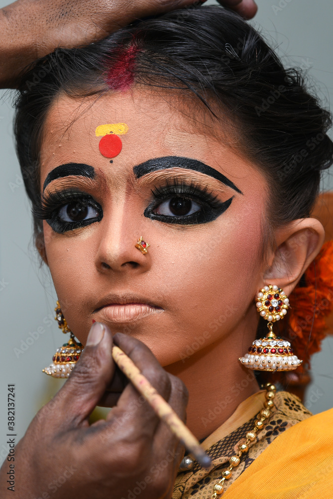 Beautiful Indian girl or women or kid doing makeup wearing sari or saree as Indian folk, classical dancer in dress for females in Kerala, India. wearing ornaments. Photo | Adobe