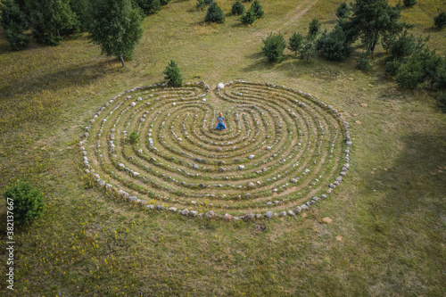 A girl meditates in the center of a spiral maze labyrinth of stones. Aerial view shooting from a drone. Esotericism  mysticism.