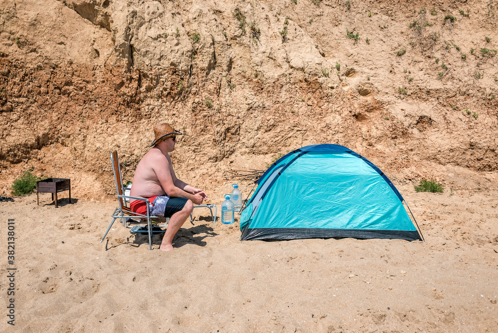 overweight man sits near blue tent overweight man sits near blue tent