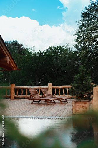 Wooden sun beds in the spa zone with swimming pool, green summer forest around, sunny summer day