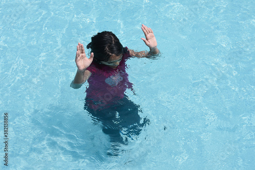 Small Indian girl swimming or learning to swim, splashing water in swimming pool in Kerala, India. Happy kid playing, diving in water.