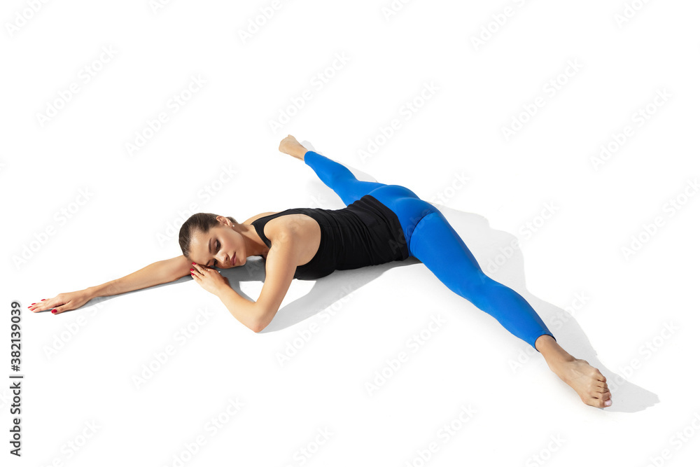 Sport. Beautiful young female athlete stretching, training on white studio background, portrait with shadows. Sportive fit model in motion and action. Flexibility, healthy lifestyle, style concept.