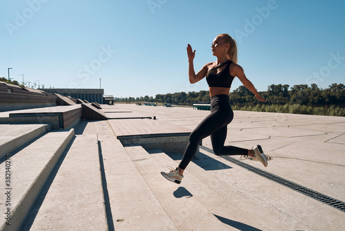 A young woman athlete runs on concrete steps. A blonde in a black suit is engaged at dawn. Healthy lifestyle. Motivation
