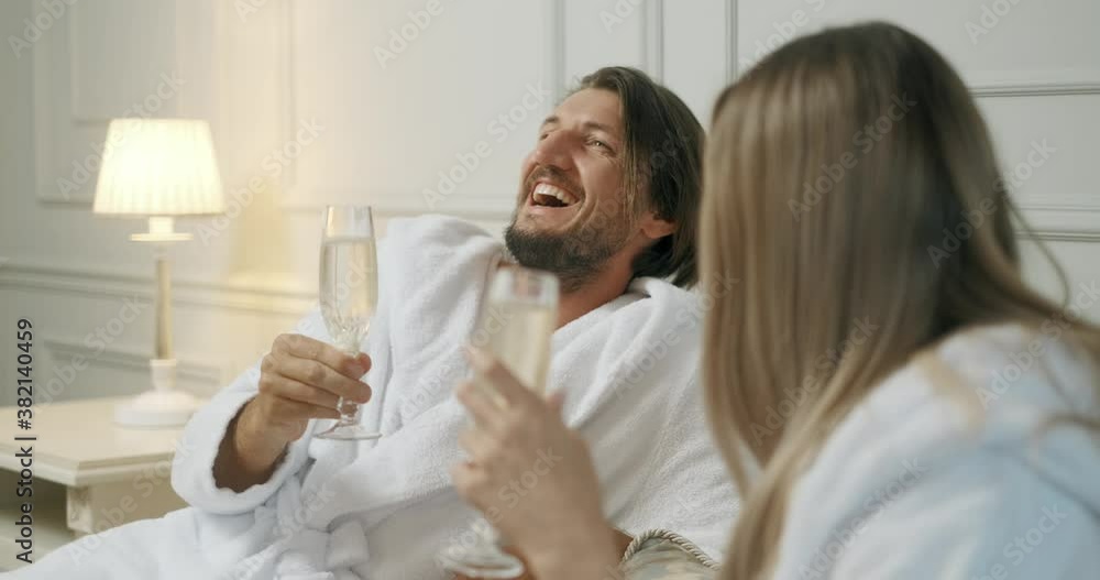 Affectionate couple toasting with champagne lying on their bed. Hotel, travel, relationships and happiness concept - smiling couple with champagne glasses in room Affectionate couple toasting with champagne lying on their bed. Hotel, travel, relationships and happiness concept - smiling couple with champagne glasses in room