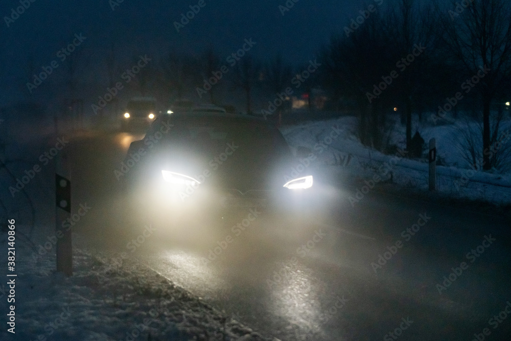 Luminous car headlights in the night in fog.