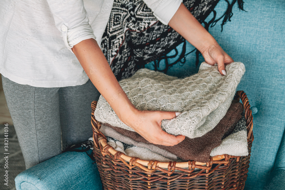 Women's hands fold a stack of warm knitted sweaters in wicker basket Women's hands fold a stack of warm knitted sweaters in wicker basket