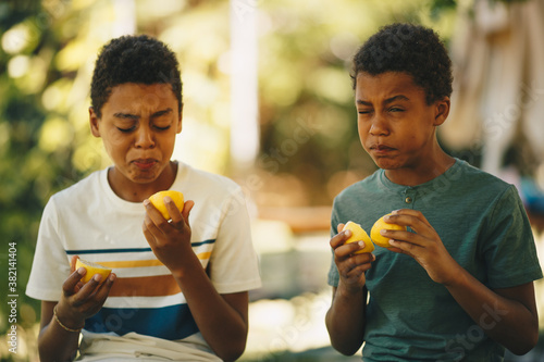Two brothers african ethnicity sitting outdoors and tasting lemon. photo