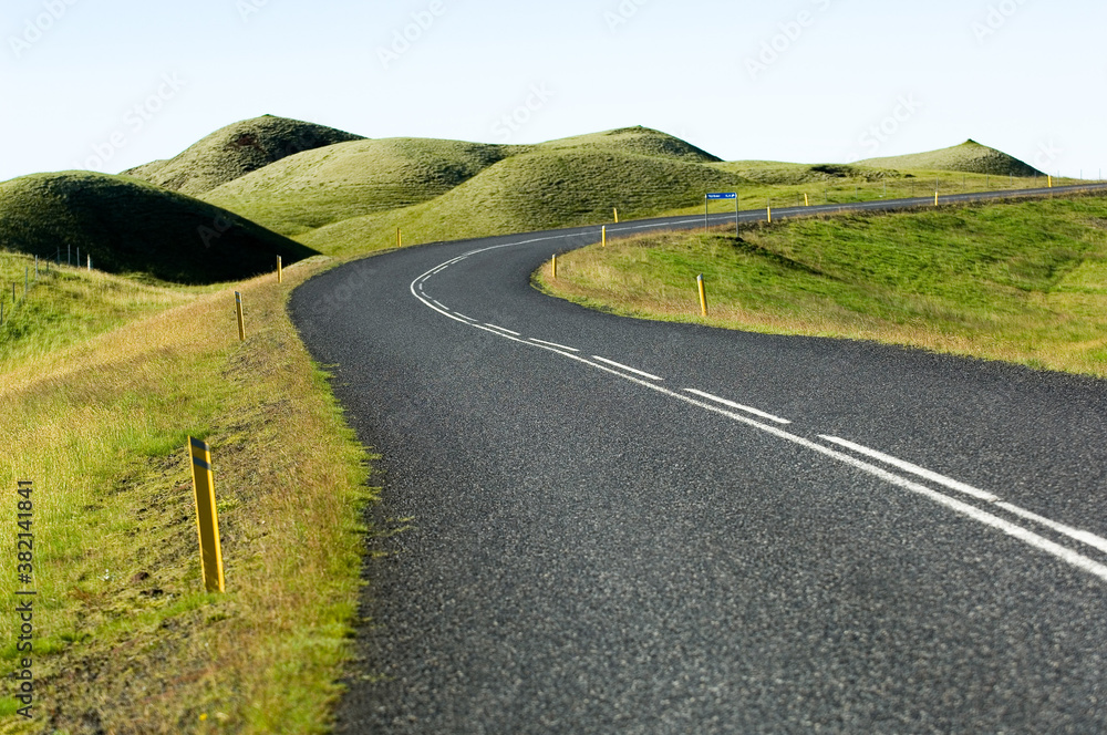 A good winding asphalted road between soft green hills.