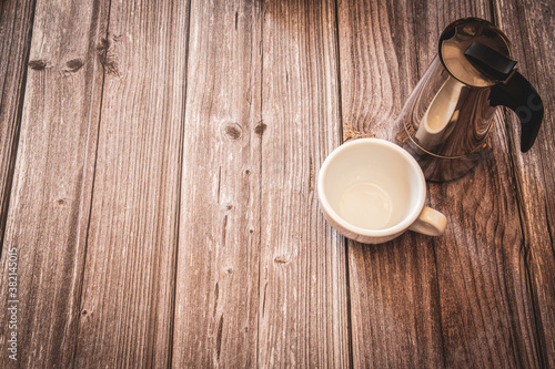 A silver coffee pot and white coffee cup on a rustic wooden background with copy space