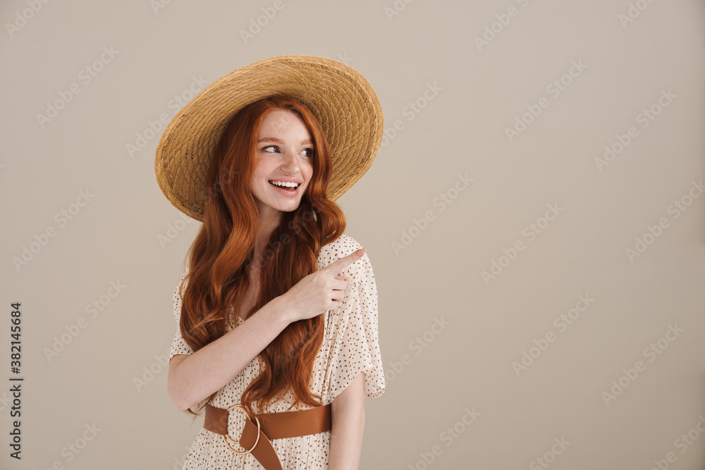 Photo of happy redhead girl in straw hat pointing finger aside