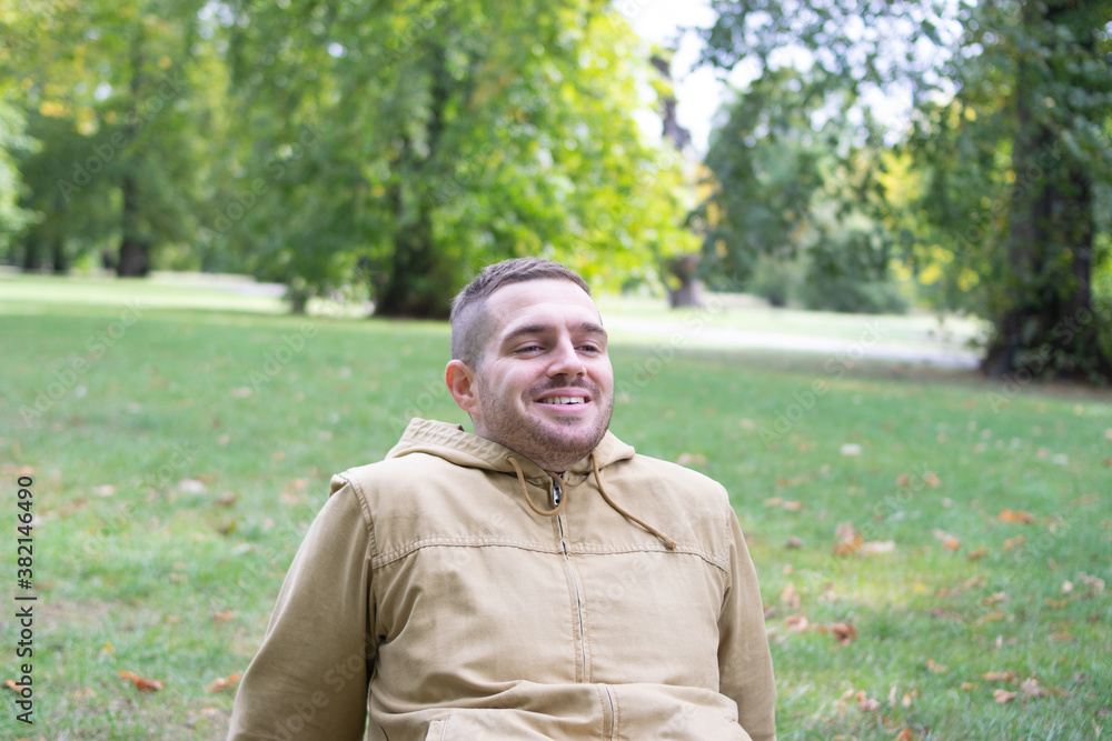 Photo of a young and attractive man sitting on the park smiling and enjoying a sunny day