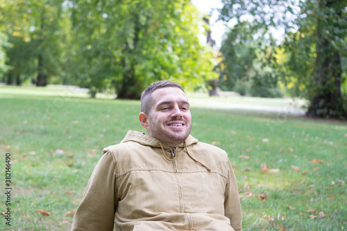 Obraz na płótnie Photo of a young and attractive man sitting on the park smiling and enjoying a sunny day w salonie