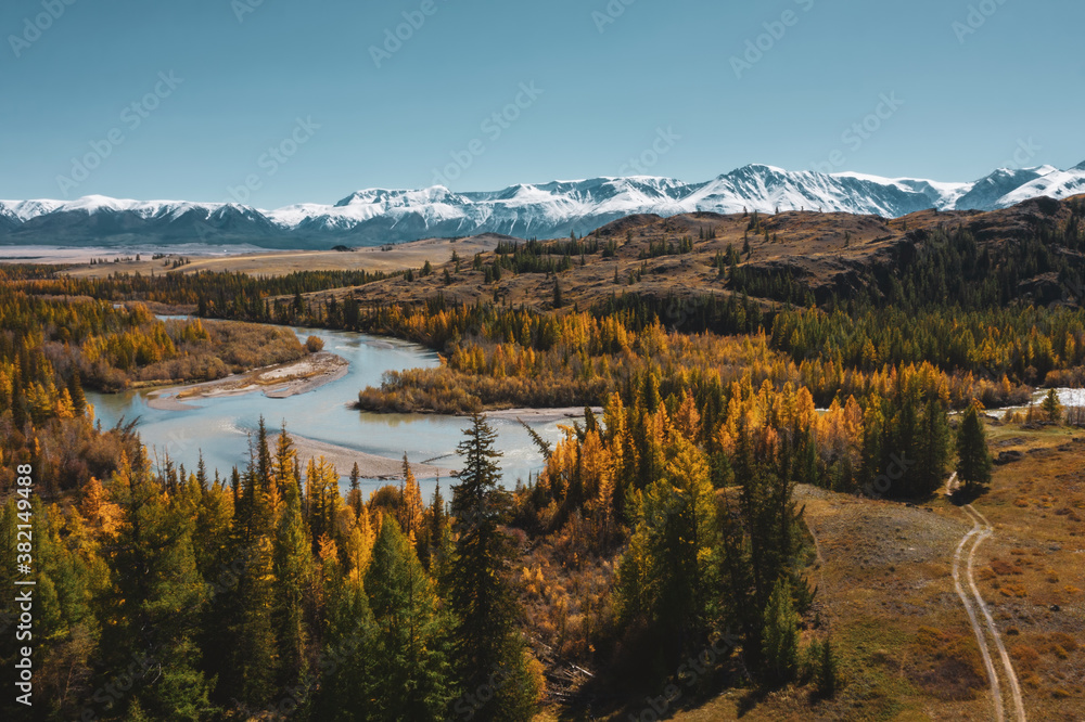 Colourful mountain valley, blue snow covered peaks, orange and green autumn forest and river. Aerial view