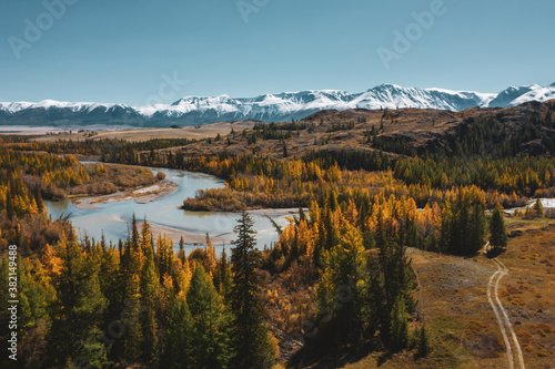 Colourful mountain valley, blue snow covered peaks, orange and green autumn forest and river. Aerial view © Annatamila